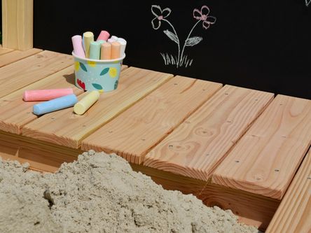 Sandkasten mit einer Tafel und bunten Kreidestücken