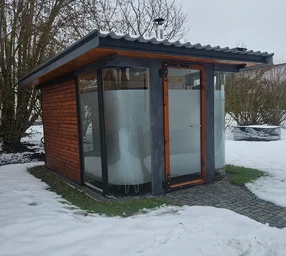 Eine moderne Außensauna mit Glasfront im verschneiten Garten.