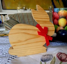 Ein hölzerner Osterhase mit einer roten Schleife steht als Dekoration auf einem Tisch.