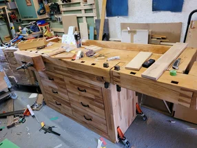 Eine hölzerne Werkbank in einer Werkstatt, bedeckt mit Werkzeugen und Holzstücken.