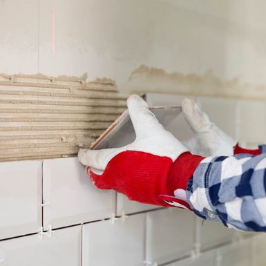 Person bringt Fliese an Wand an