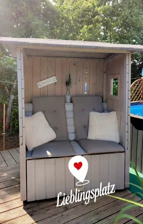 Ein selbstgebauter Strandkorb aus Holz mit Kissen und dem Schriftzug 'Lieblingsplatz'.