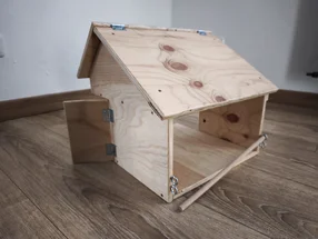 Ein selbstgebautes Vogelhaus aus Holz auf einem Holzboden.