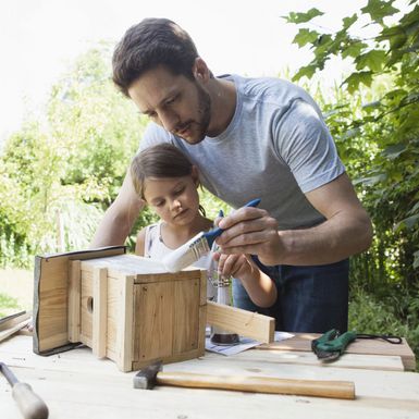 Person und Kind streichen ein Vogelhaus