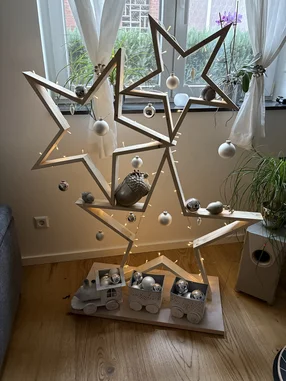 Moderner Weihnachtsbaum aus Holzsternen, dekoriert mit Kugeln und einer Lichterkette.