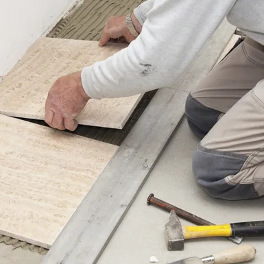 Person verlegt Fliesen mit Gummihammer