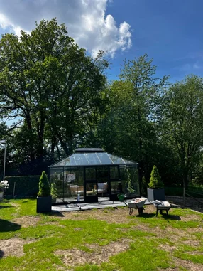 Ein modernes, schwarzes Glashaus in einem Garten, davor stehen zwei Schubkarren.