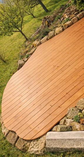 Eine geschwungene Holzterrasse, die von Natursteinen und einer Wiese umgeben ist.