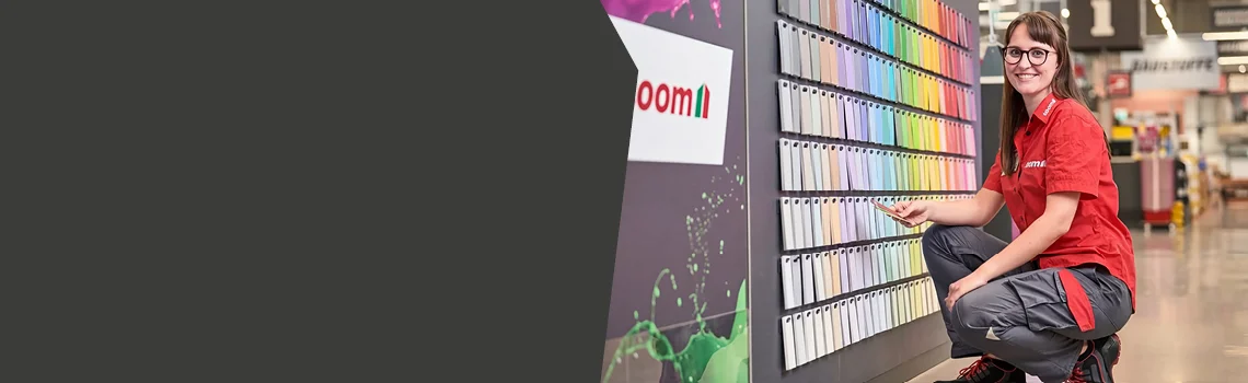 Person kniet lächelnd vor einer Wand mit vielen bunten Farbmustern